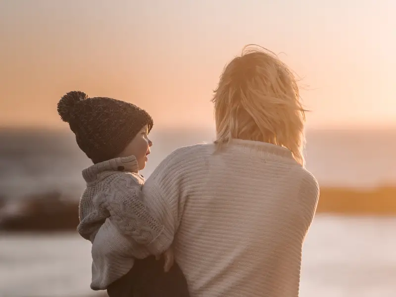 une mère portant son petit garçon à l'extérieur au coucher du soleil